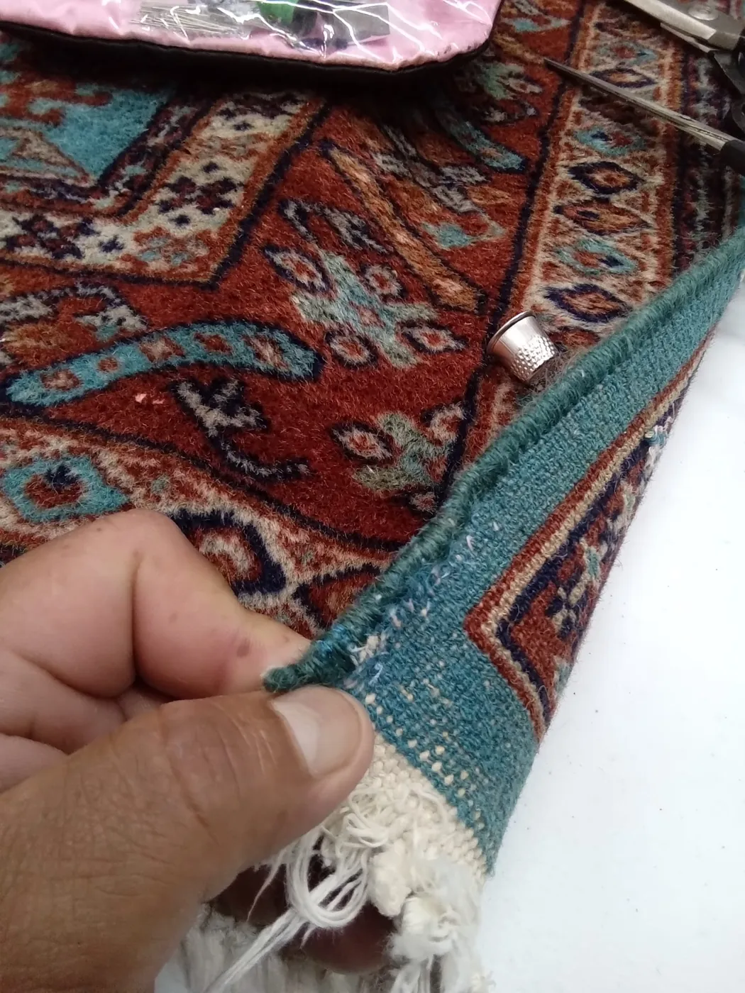 Hands securing the fringe of a red and teal rug